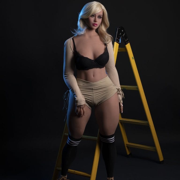 Blonde sex doll with realistic features standing next to ladder against dark background.