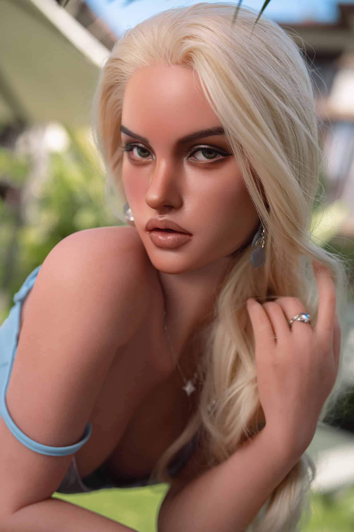 Realistic female doll with blonde hair and captivating eyes outdoors.