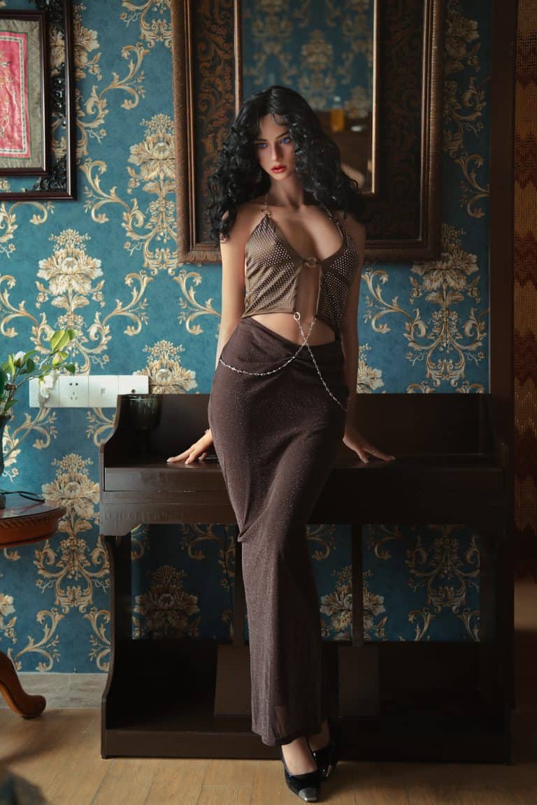 Seductive female doll in stylish evening outfit with dark hair posing indoors.