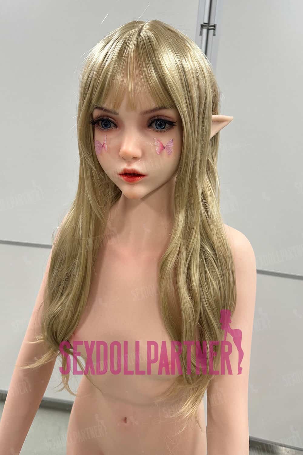 Silicone sex doll with elf ears, blonde hair, butterfly face tattoos, and realistic features.
