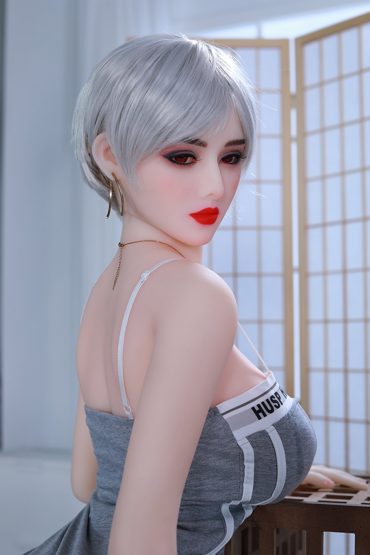 Realistic sex doll with silver hair, red lips, and fashionable jewelry in a modern room.