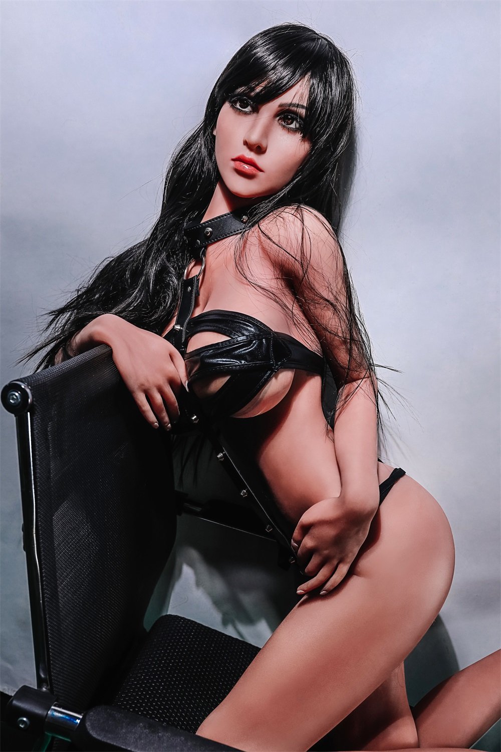 Realistic sex doll in leather outfit with black hair, posed seductively on chair for adult pleasure imagery.