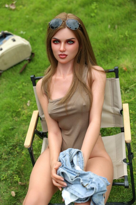 Silicone doll woman sitting outdoors on a camping chair in a grassy area.