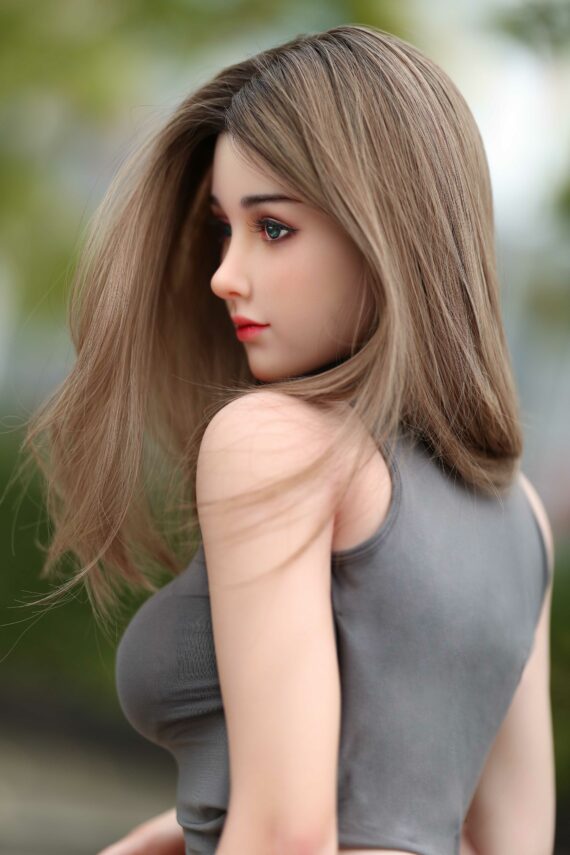 Realistic female doll with long brown hair and detailed features, outdoor setting.