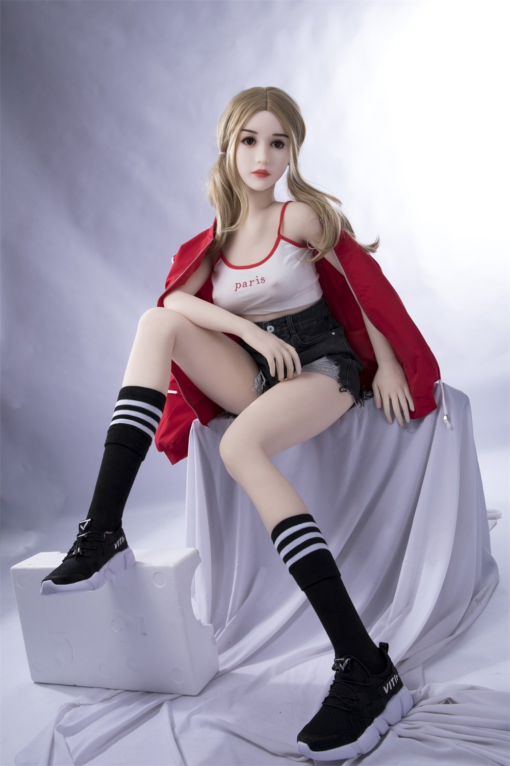 Realistic sex doll in casual streetwear, sitting on a white fabric setup. Perfect for anime, cosplay, or adult novelty displays.