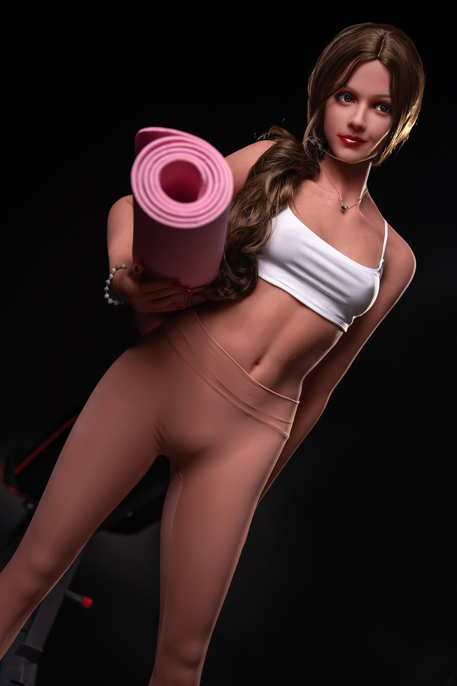 Pink yoga mat held by realistic sex doll with long brown hair and athletic outfit on black background.