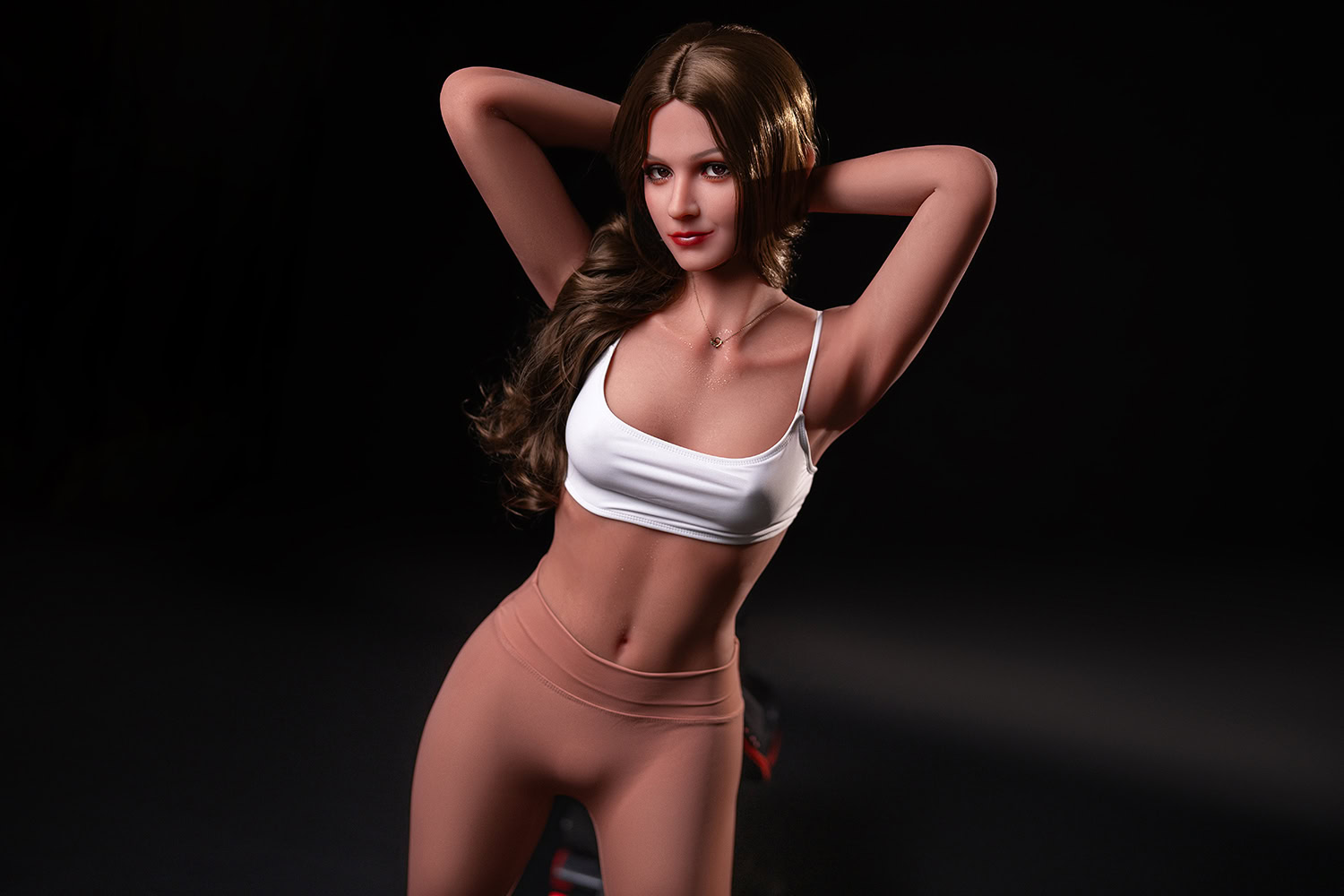 Realistic female sex doll posing in a studio with black background, wearing a white crop top and pink leggings.