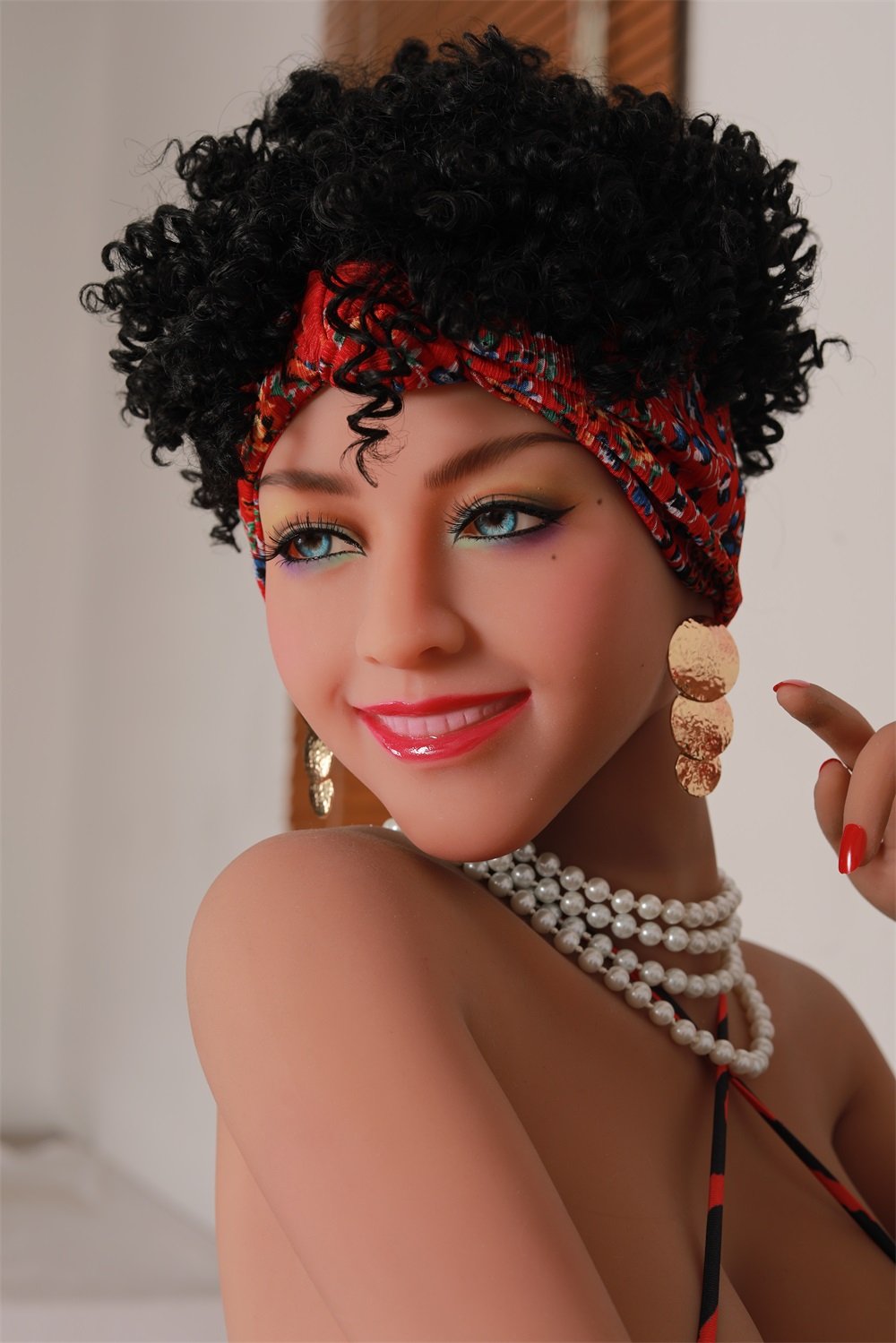 Bright blue-eyed doll with curly black hair, wearing a colorful headscarf and pearl jewelry, in a close-up portrait.