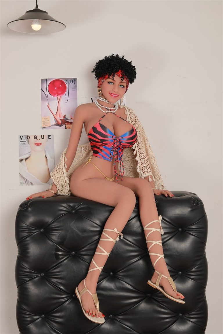 Busty sex doll dressed in colorful bikini with laced-up front, lace shawl, and gladiator sandals lounging on black leather sofa.