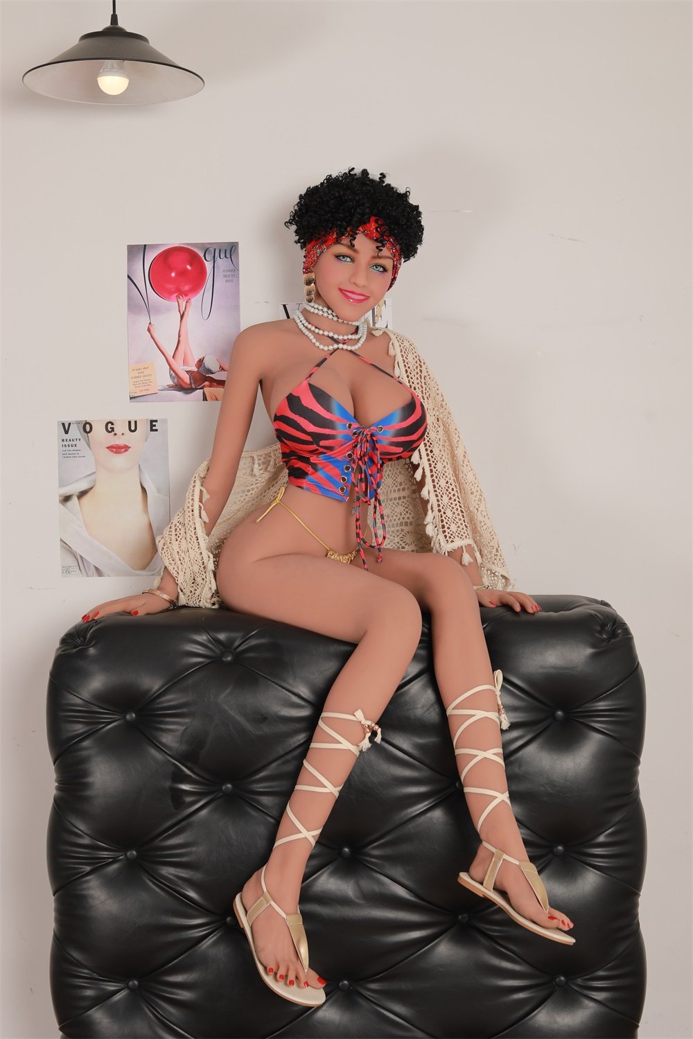 Busty sex doll dressed in colorful bikini with laced-up front, lace shawl, and gladiator sandals lounging on black leather sofa.