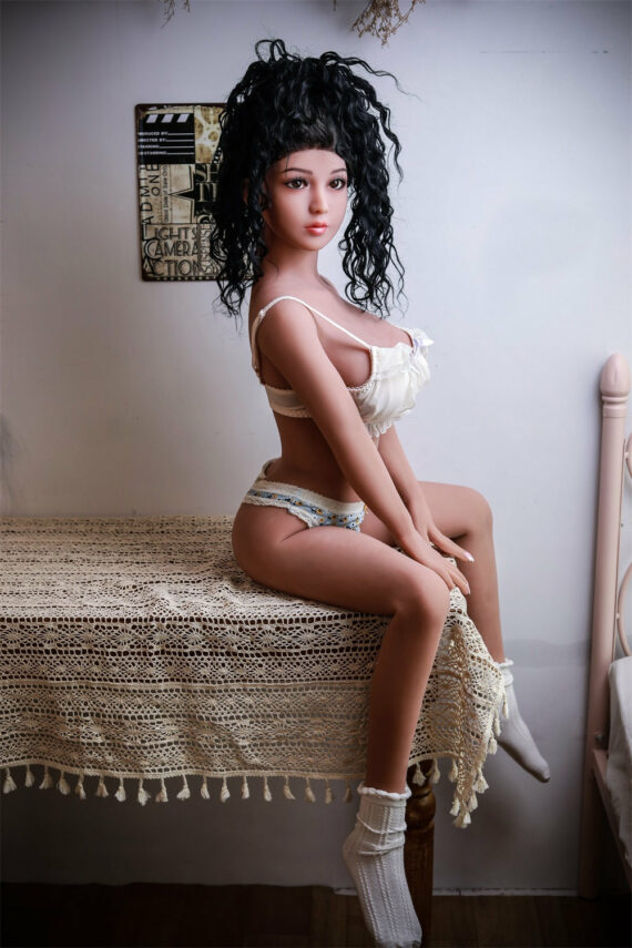 Seducedoll realistic sex doll lying on bed with crochet blanket, soft lighting, detailed features.