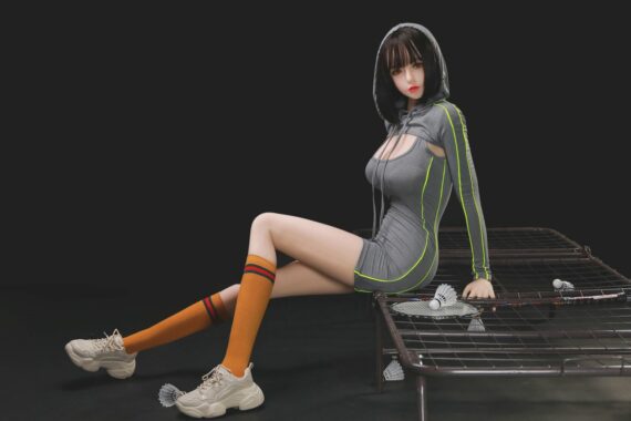 Realistic sex doll girl sitting on a bed with a dark background, dressed in sporty attire.