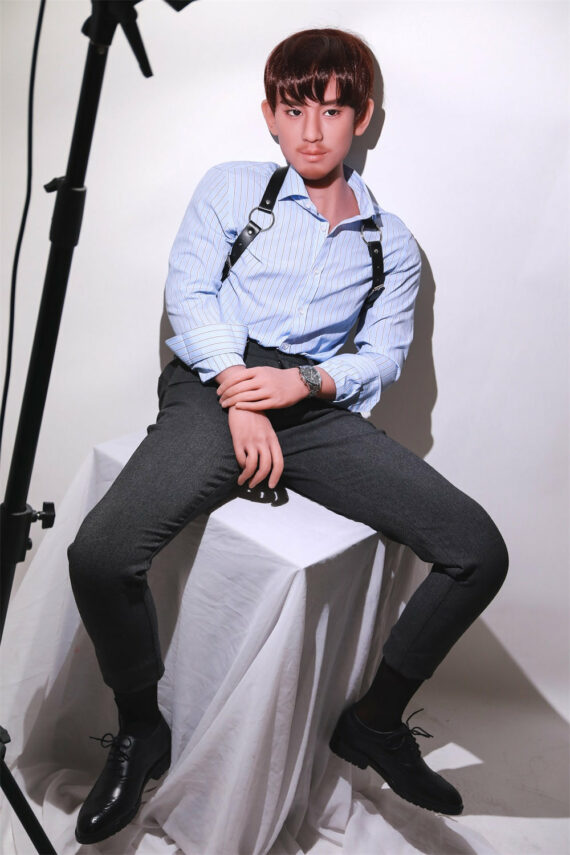 Boy with short brown hair wearing formal outfit sitting on white cloth-covered platform under studio lighting.