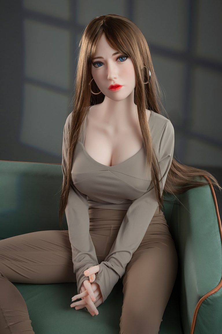 Realistic sex doll sitting on green sofa, detailed face with blue eyes, long brown hair, wearing beige outfit.