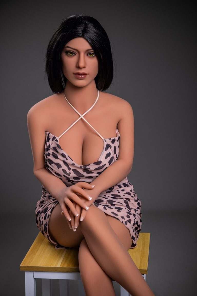 Realistic female doll wearing leopard print dress, sitting on a wooden stool, showcasing detailed craftsmanship.