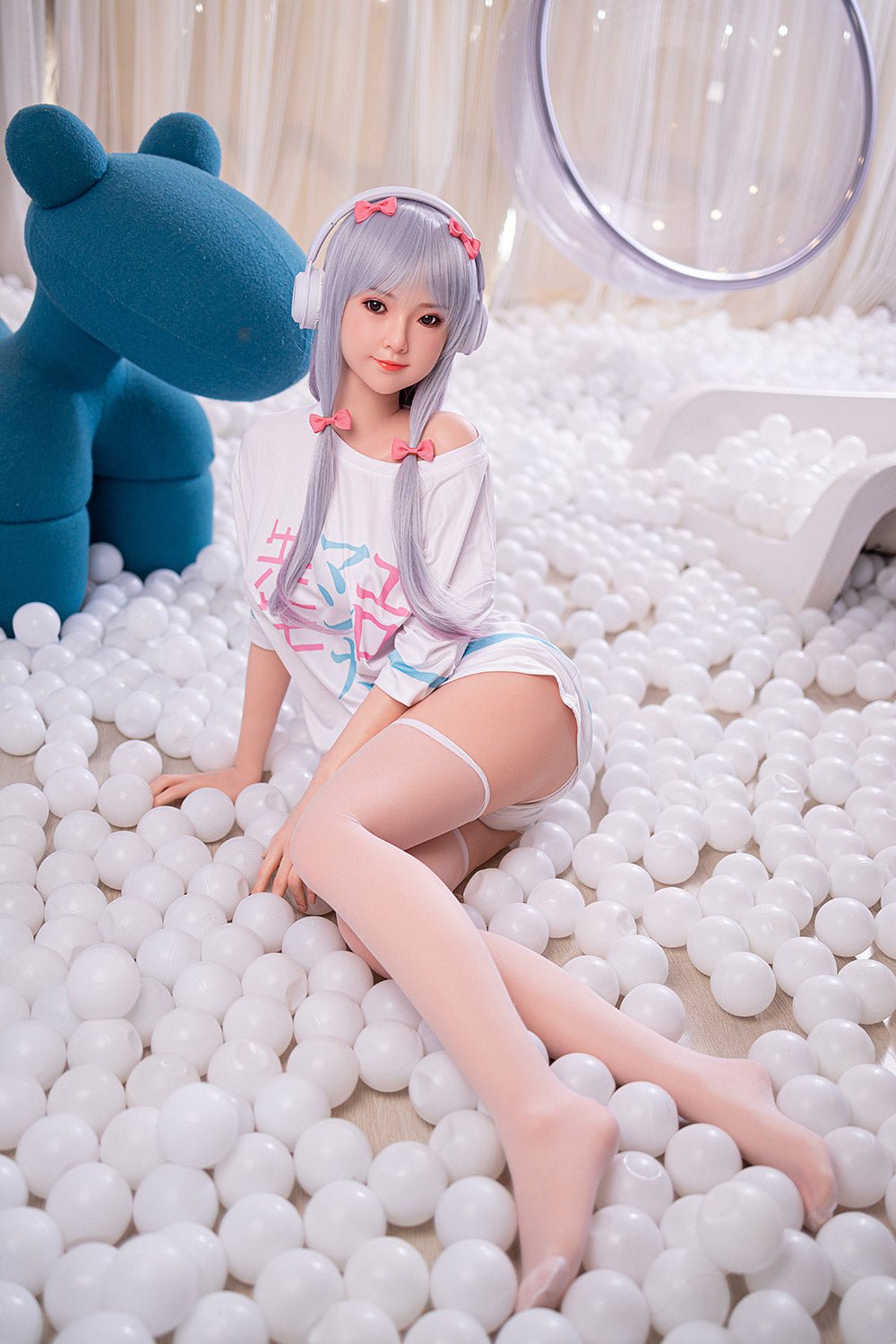 Soft-bodied doll surrounded by white balls, cute anime-style face, pastel-colored wig, in a playful setting.
