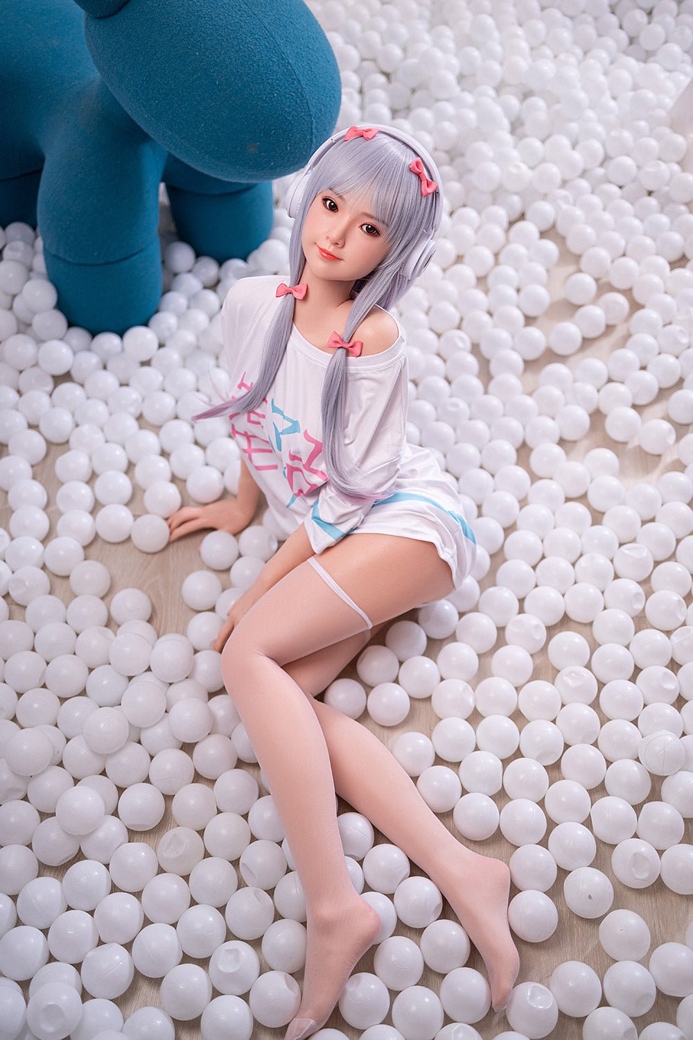 Realistic anime-style love doll with long silver hair, wearing headphones and casual clothing, surrounded by white plastic balls.