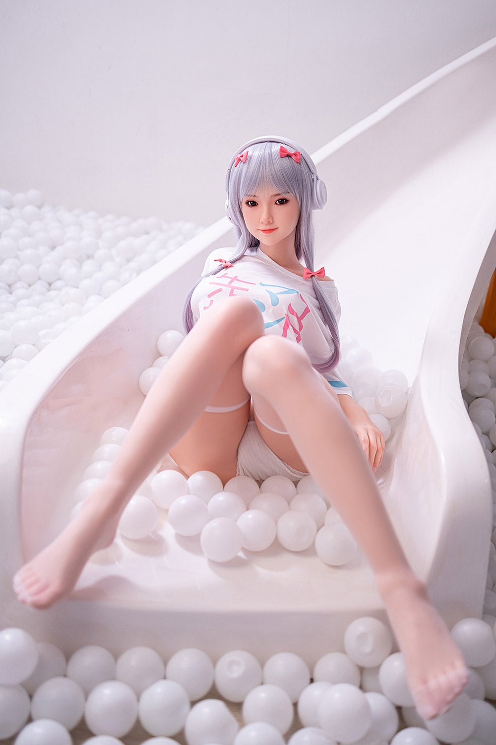 Cute anime-style doll wearing headphones in a ball pit with white plastic balls.