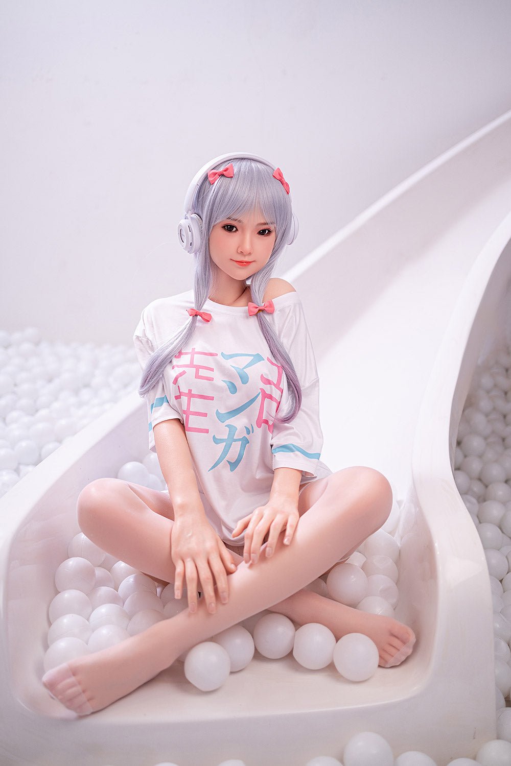 Soft anime-style doll with silver hair, pink bows, wearing a Japanese-themed T-shirt, sitting in a white ball pit with a slide.