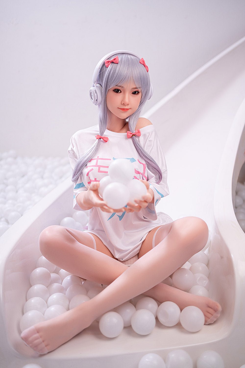 Cute anime-style sex doll with silver hair, pink bows, and headphones, sitting in ball pit, playful and realistic look.