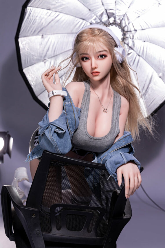 Realistic female doll with blonde hair posing in studio photo shoot under professional lighting.
