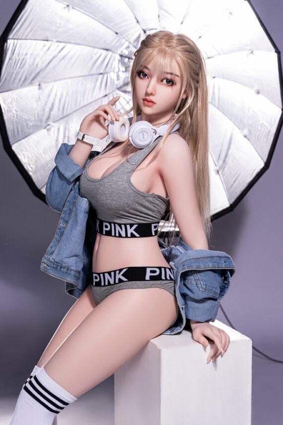 Realistic sex doll girl with blonde hair holding headphones under studio umbrella, dressed in Pink sportswear and denim jacket.