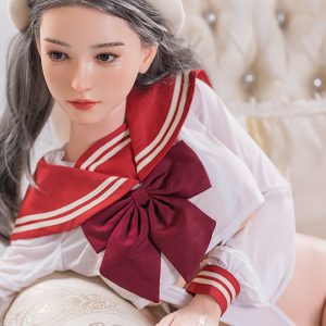 Seductive doll girl in schoolgirl outfit on luxurious bed.