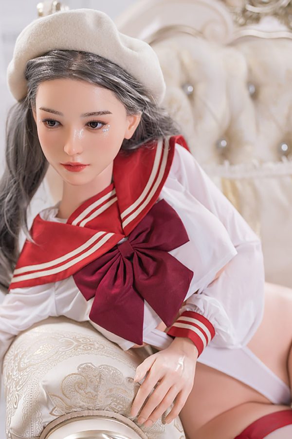 Seductive doll girl in schoolgirl outfit on luxurious bed.
